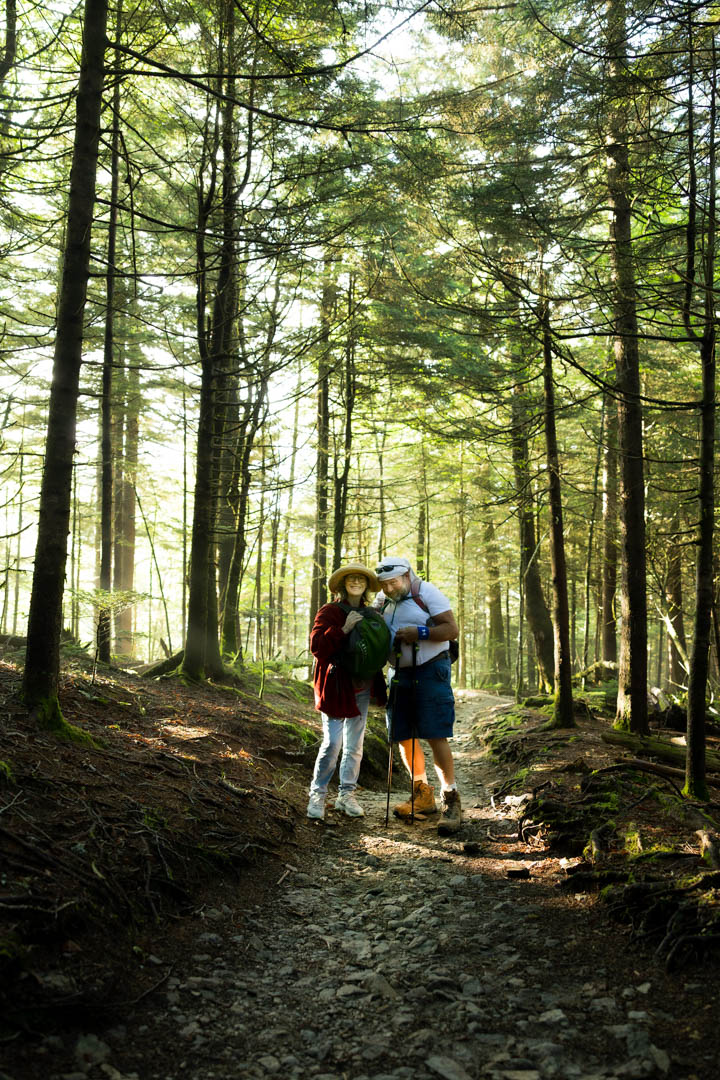 Couple hiking through wind-brushed meadow at Andrews Bald during sunrise